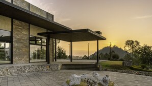 A modern building with a stone facade and large windows, a covered outdoor area with steps, and a landscaped garden with rocks and grass. - Hotel Rocaval (San Cristóbal de las Casas)
