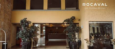 Entrada del hotel Rocaval San Cristobal & Casas, con mostrador de recepción, plantas en macetas grandes y un muro de piedra.