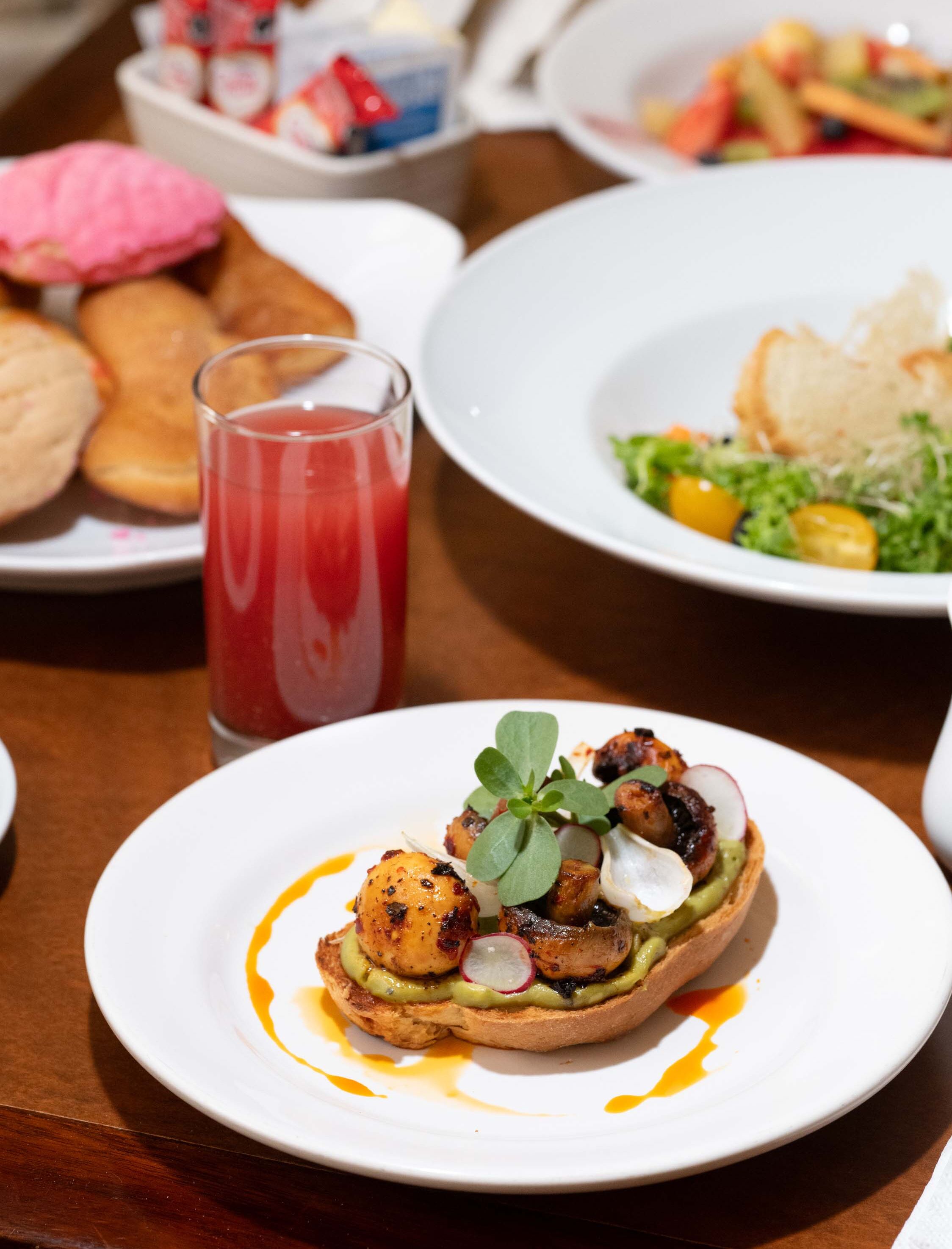 A dining table with plates of food, including a dish with grilled chicken, avocado, and radish, and a glass of red beverage.