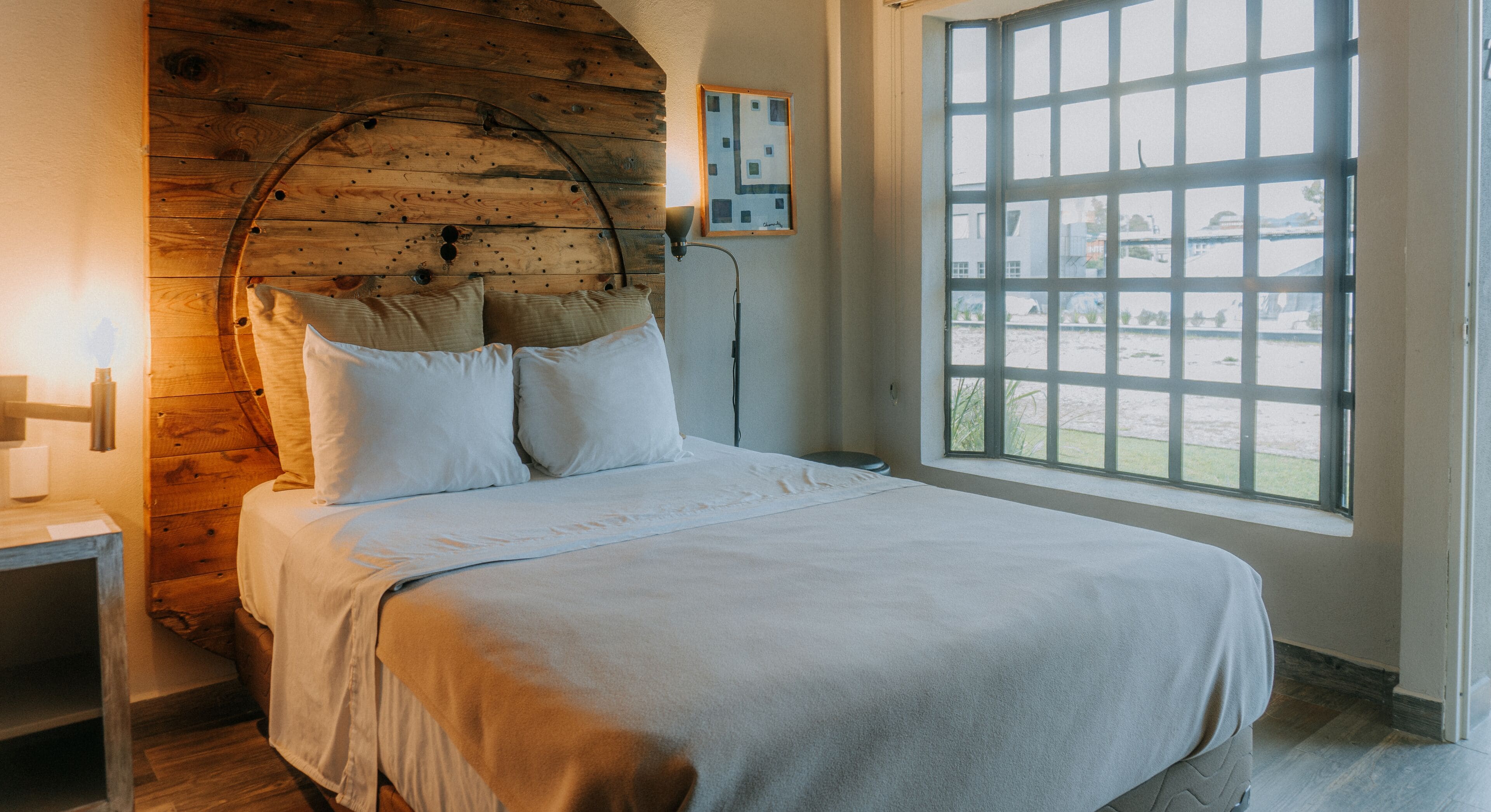 A bedroom with a wooden headboard, a large window, and a view of the outside.