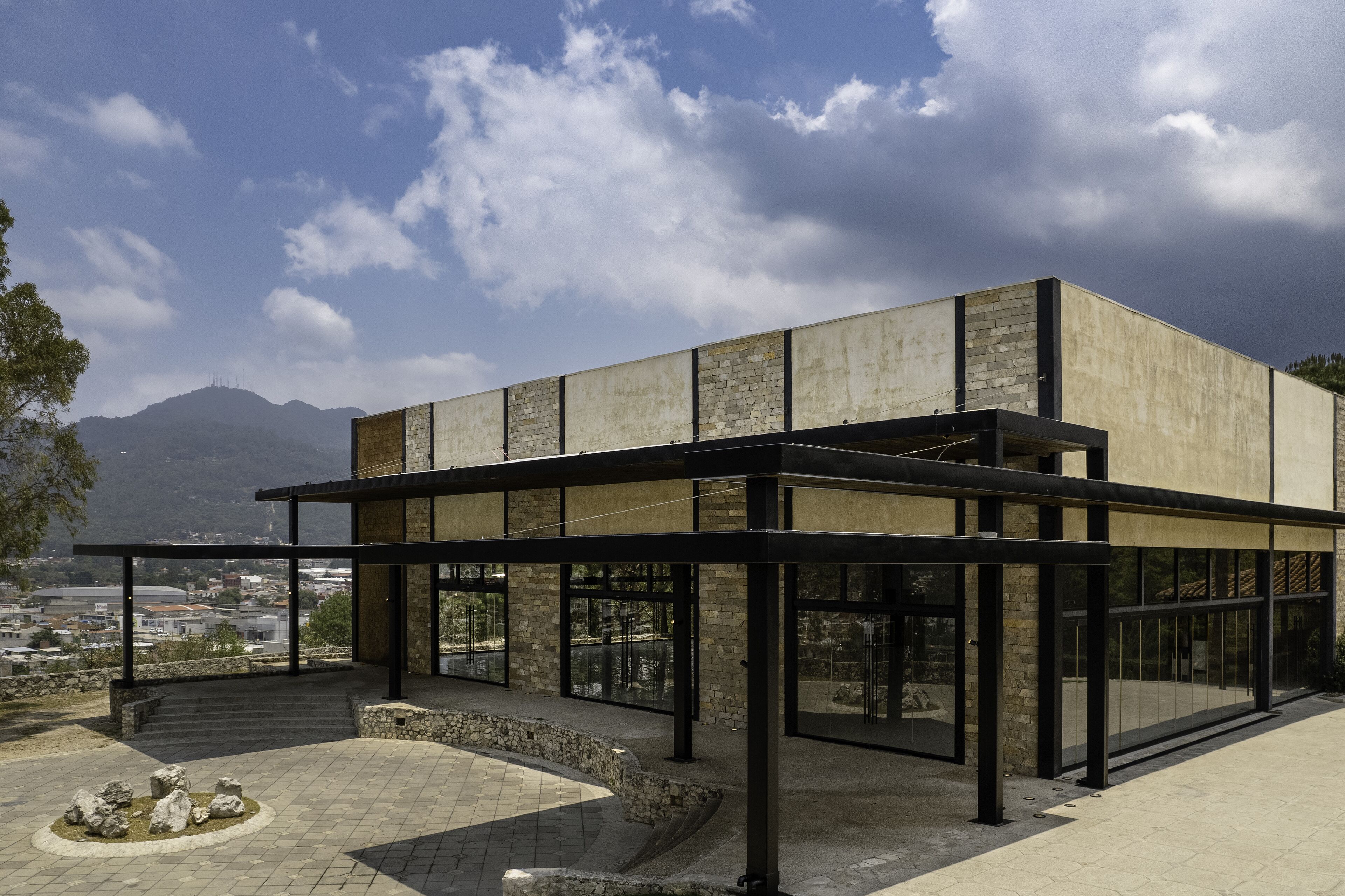 Un edificio moderno con fachada de vidrio, detalles de piedra y vistas a un paisaje montañoso.