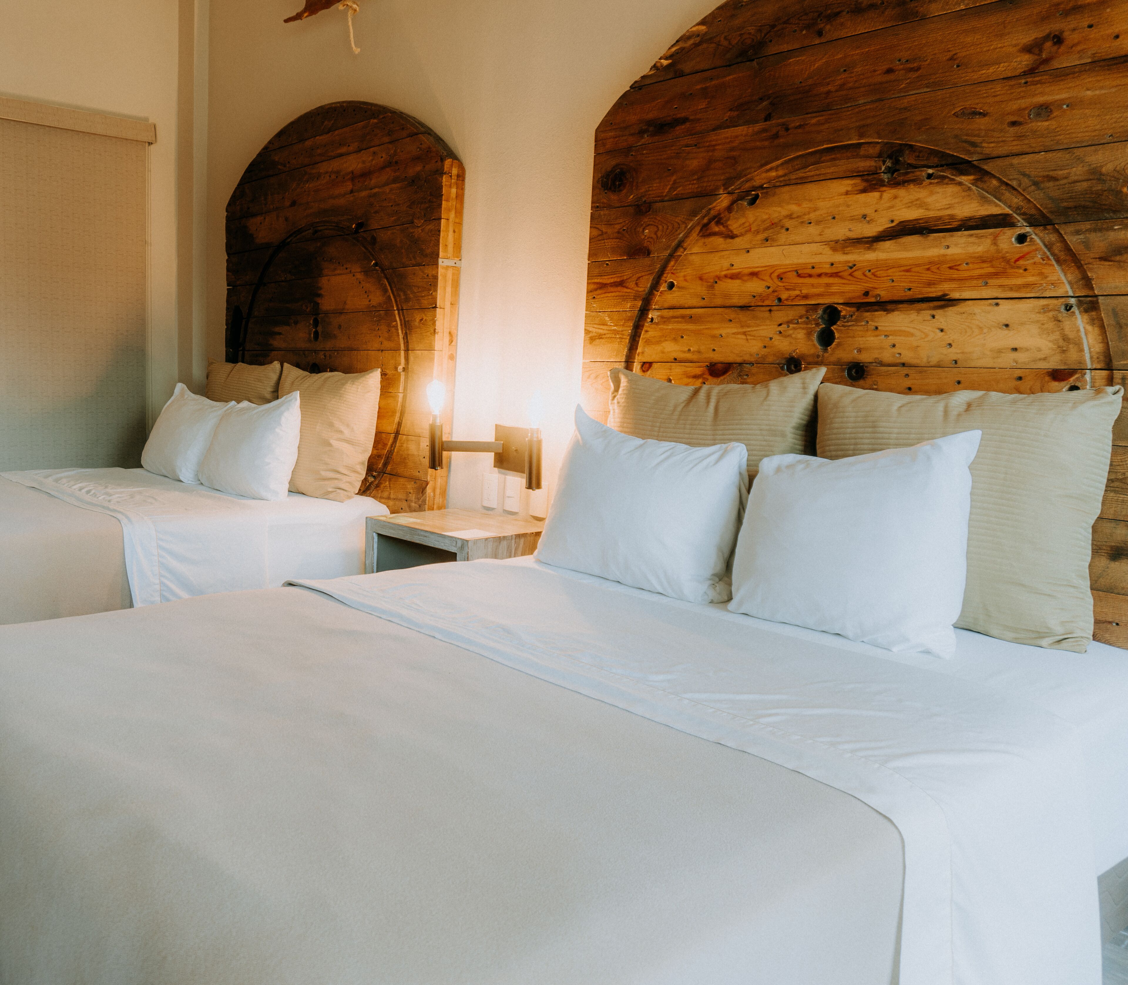 Ein Zimmer mit zwei Betten, Holz-Kopfteilen und einem Nachttisch mit Lampe.