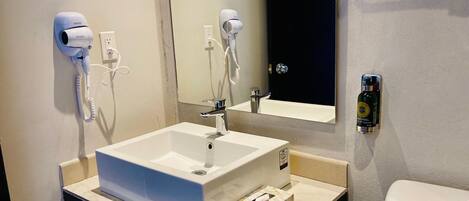 A bathroom with a white sink, a mirror, a hairdryer, a bottle of hand soap, and a towel dispenser.
