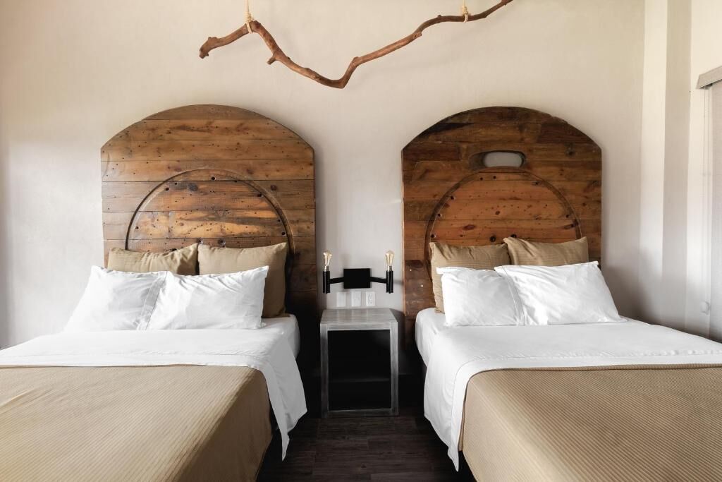 A room with two beds, wooden headboards, a small bedside table, and a hanging branch.