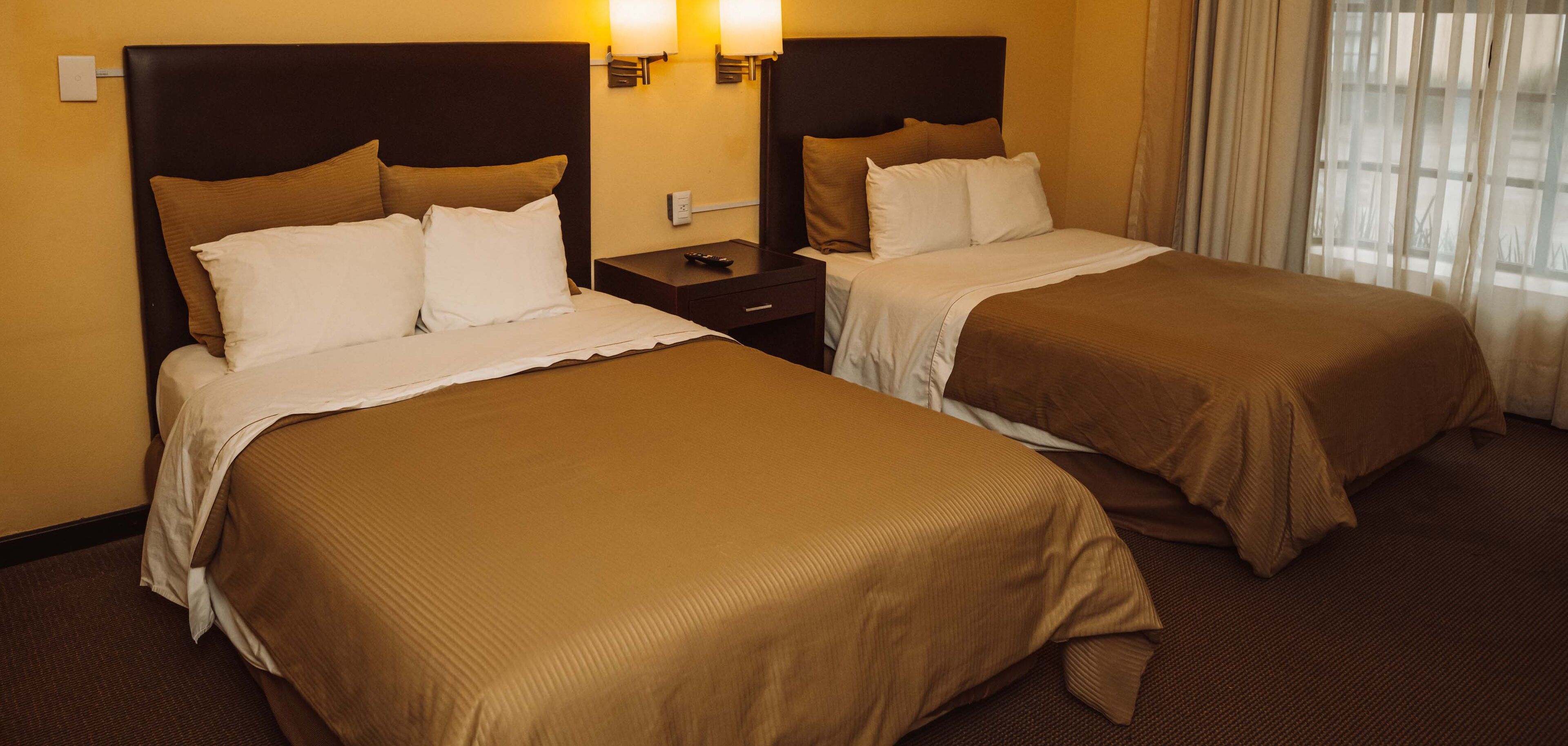 Een hotelkamer met twee eenpersoonsbedden, elk met hoofdeinde, nachtkastjes en lampen.