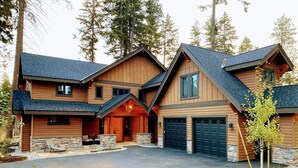 Une grande maison en bois à plusieurs étages, dotée d’un garage, de fondations en pierre et d’une allée.