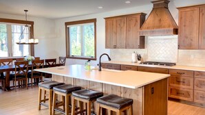 Une cuisine spacieuse avec des meubles en bois, un grand îlot central doté de tabourets et une vue sur l’extérieur grâce à de grandes fenêtres.
