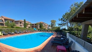 Une piscine entourée de bâtiments et d’arbres, avec des chaises longues et une chaise rouge.