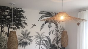 Un dormitorio con cama, mesita de noche, un mural de plantas tropicales y una lámpara colgante.