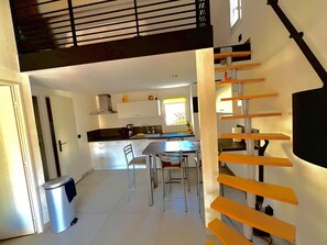 Une cuisine moderne avec des meubles blancs, un coin repas comprenant une table et des chaises, et un escalier avec des marches en bois.