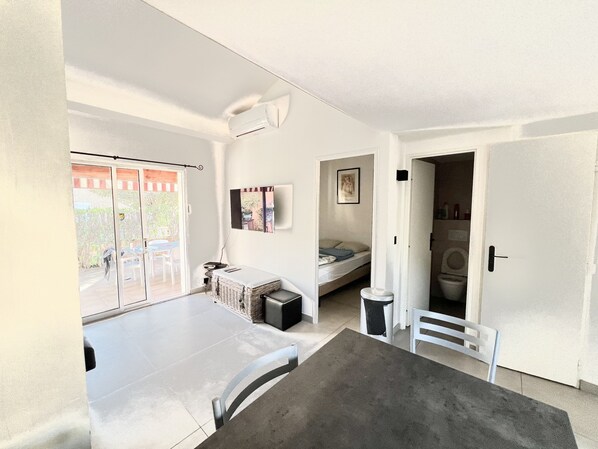 Un espace de vie compact comprenant un balcon, un lit, une petite table et un lave-linge.