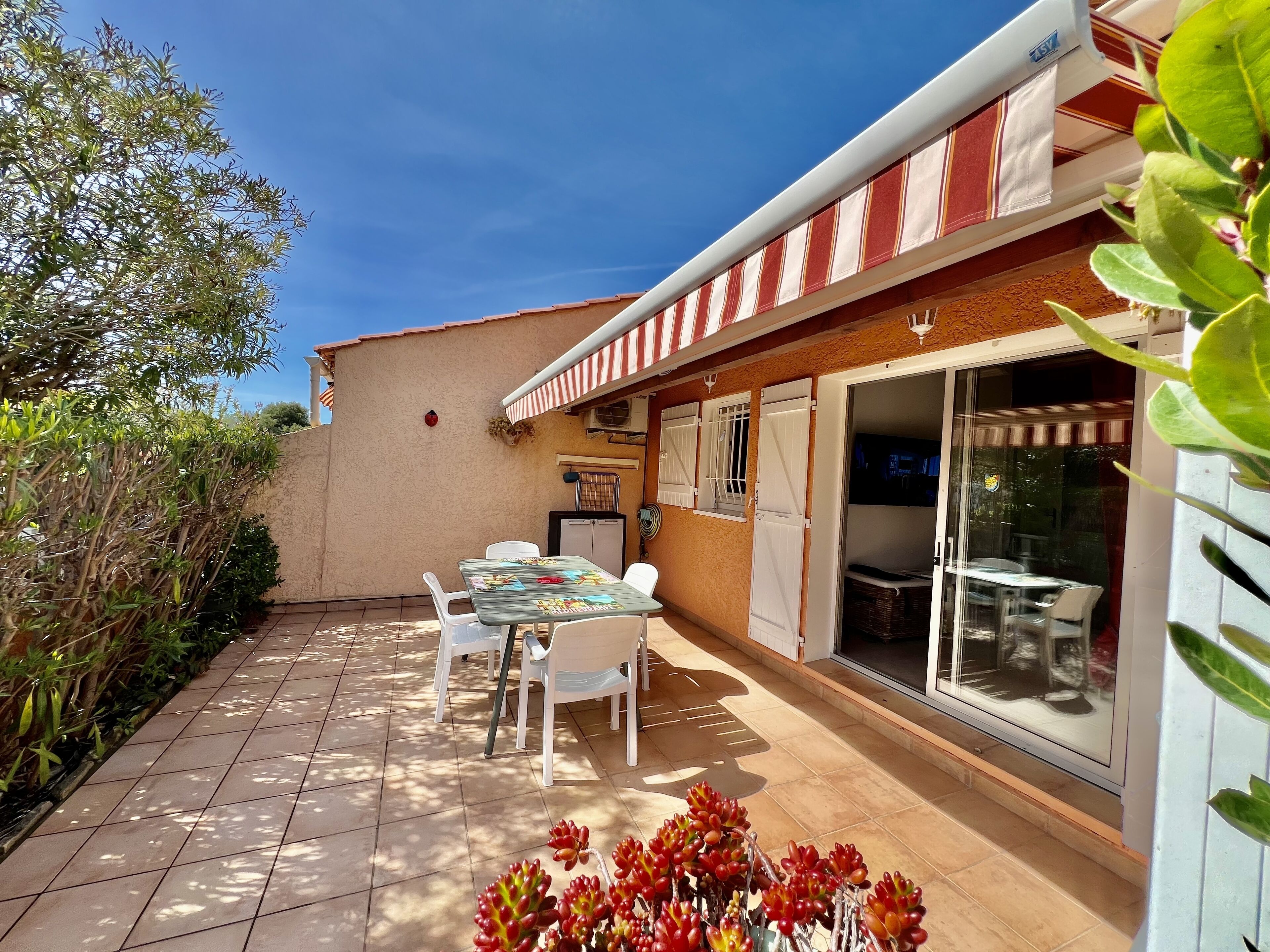 Une terrasse avec une table et des chaises, une porte-fenêtre coulissante et un petit réfrigérateur.