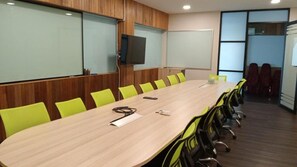 Un salón de conferencias con una larga mesa, sillas verdes, un televisor y una pizarra.
