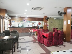 A restaurant with a brick wall, a counter, and tables with red tablecloths. - Hotel Damai (Parit Buntar)