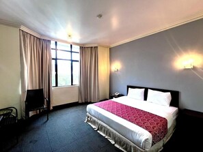 A hotel room with a bed, a desk, a chair, a window with curtains, and wall-mounted lights. - Hotel Damai (Parit Buntar)
