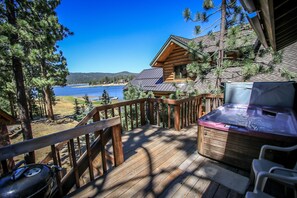 Um deck de madeira com hidromassagem, com vista para um lago e uma cabana.