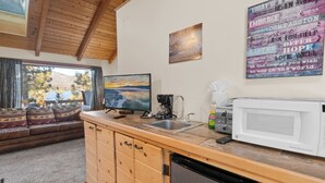 A cozy cabin interior with a wooden dining area, a kitchen with a sink and microwave, and a large window offering a scenic view.