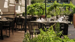 An outdoor dining area with wicker chairs and tables, potted plants, and a building in the background. - Hotel Alden Splugenschloss Zurich - Leonardo Limited Edition (Zürich)