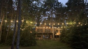 Een gebouw met twee verdiepingen, een terras, omringd door bomen en lichtslingers.