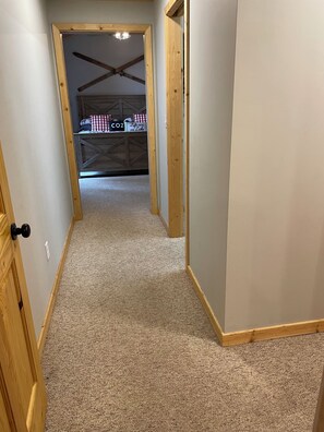Un pasillo con piso alfombrado que conduce a una habitación con techo de madera y una lámpara visible.