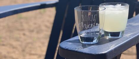 Una silla de playa con dos vasos de una bebida clara sobre una mesa.