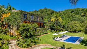 A house with a swimming pool, surrounded by lush greenery and a stone staircase.