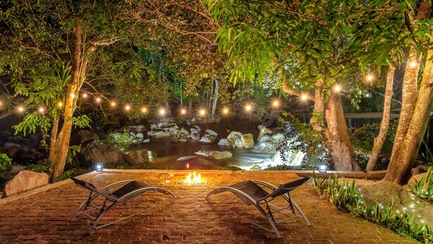 A patio with a fire pit, two lounge chairs, and a pond with a waterfall.