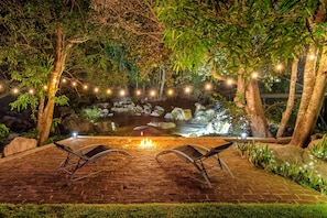 A patio with a fire pit, two lounge chairs, and a pond with a waterfall.