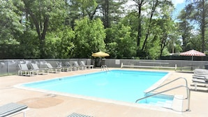 A rectangular swimming pool with a metal ladder and a metal railing. There are lounge chairs and an umbrella near the pool. - Lake Aire Motel (Wisconsin Dells)