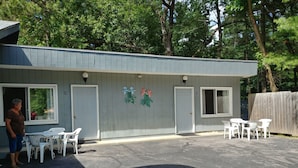 A small building with two doors, a patio area with white plastic chairs, and a parking lot. - Lake Aire Motel (Wisconsin Dells)