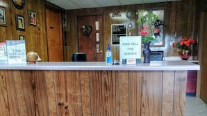 A wooden reception desk with a sign for ring bell service, framed pictures on the wall, and a vase with flowers. - Lake Aire Motel (Wisconsin Dells)