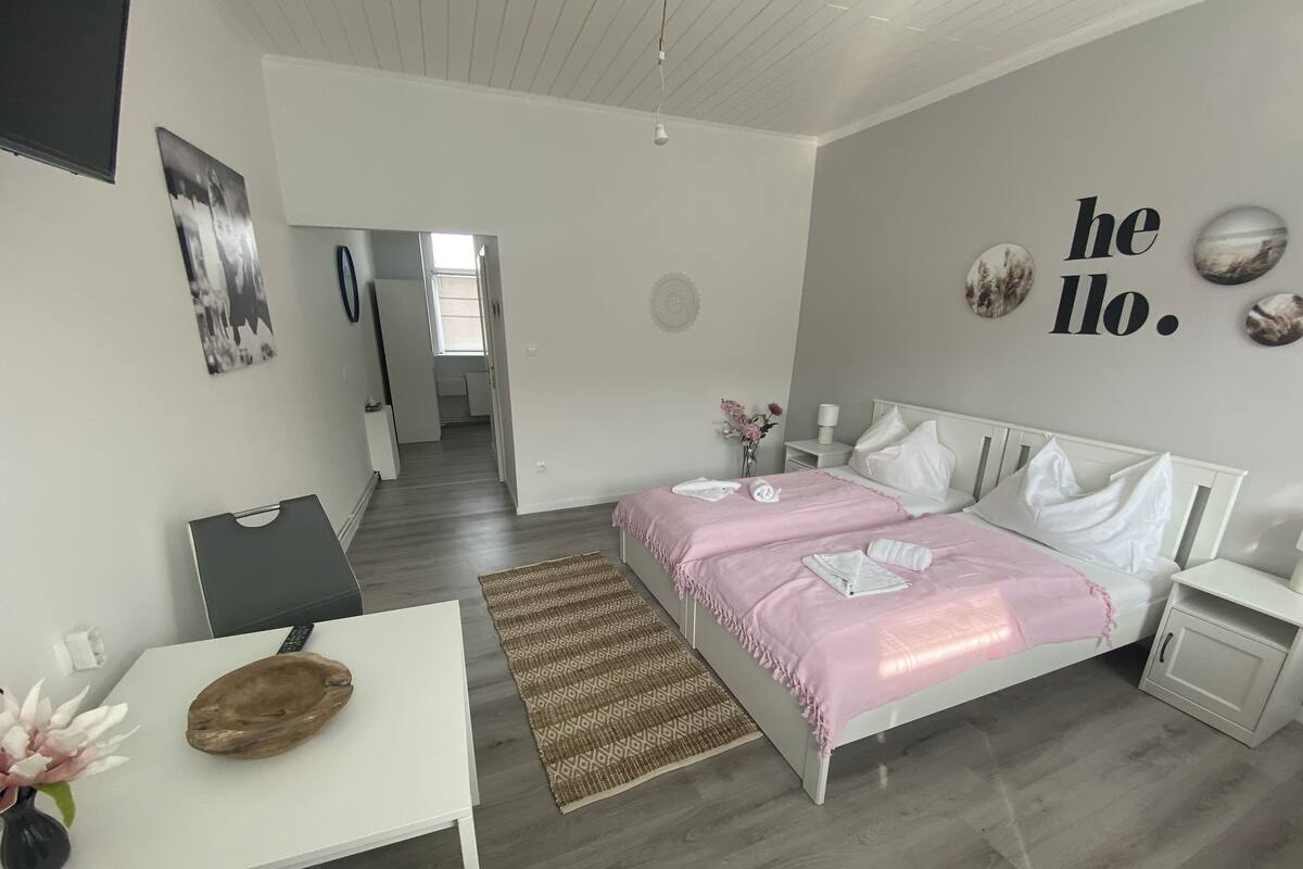 Une chambre moderne avec un lit, des tables de chevet, un bureau et une chaise. Un couloir mène à une autre pièce.