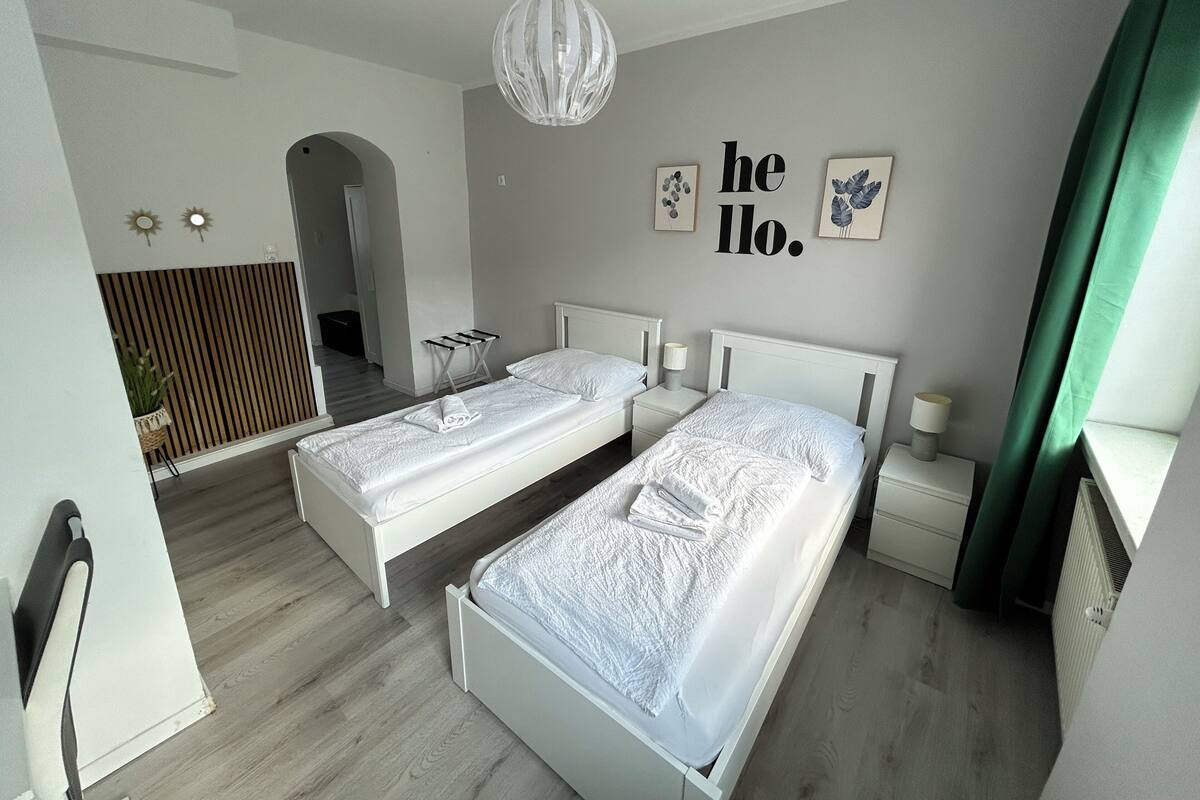 Une chambre moderne avec deux lits, un luminaire suspendu et un panneau mural sur lequel est écrit « Bonjour ».