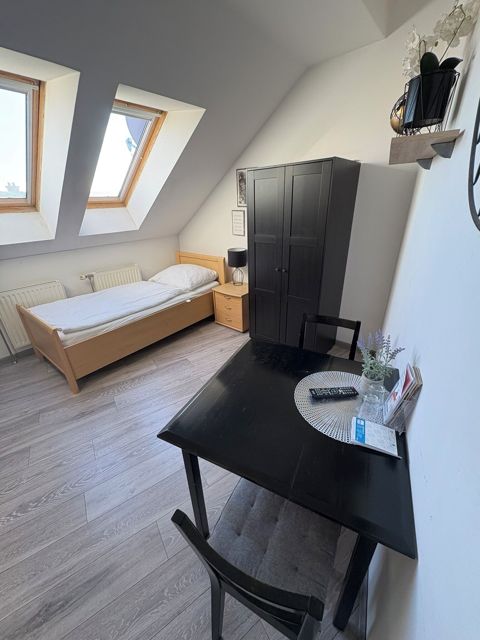 A compact bedroom with a bed, a desk, and a chair. There are skylights and a radiator.