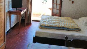 A bedroom with a bed, a desk with a TV, a window with curtains, and a ceiling fan.