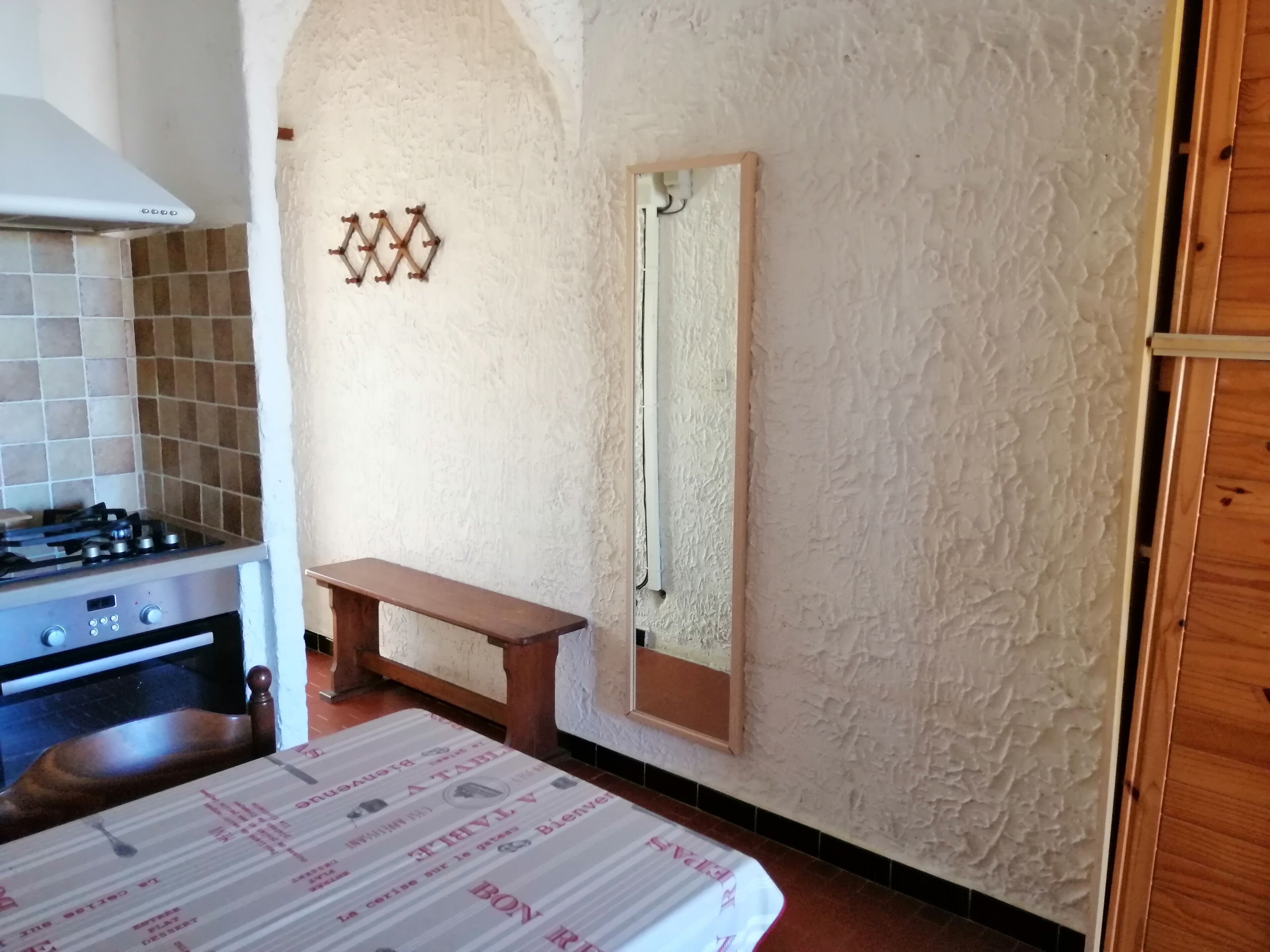 A kitchen with a stove, a wooden bench, and a wall-mounted mirror.