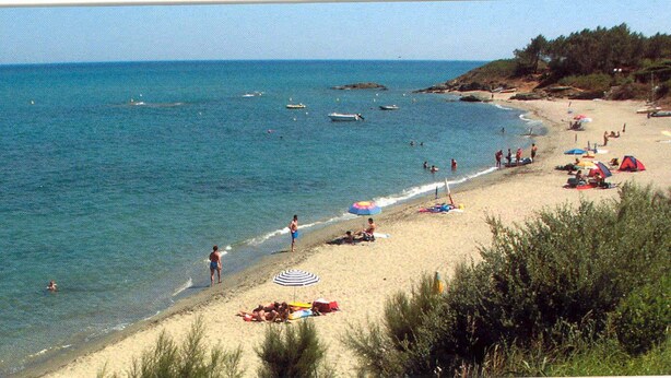 A beach with people sunbathing, swimming, and boats in the water.