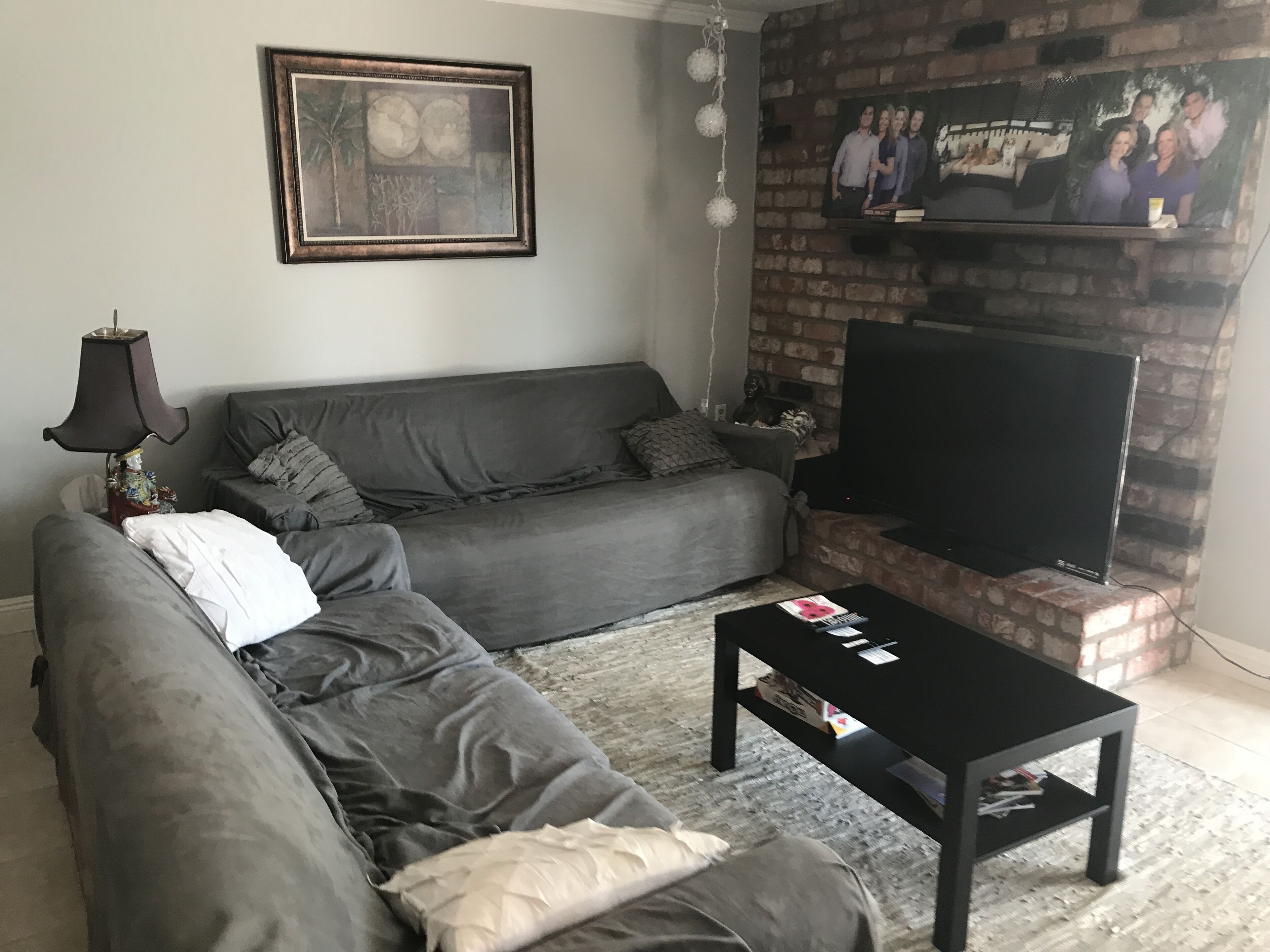 A living room with a grey sofa, a black coffee table, a fireplace, and a flat-screen TV mounted on the wall.