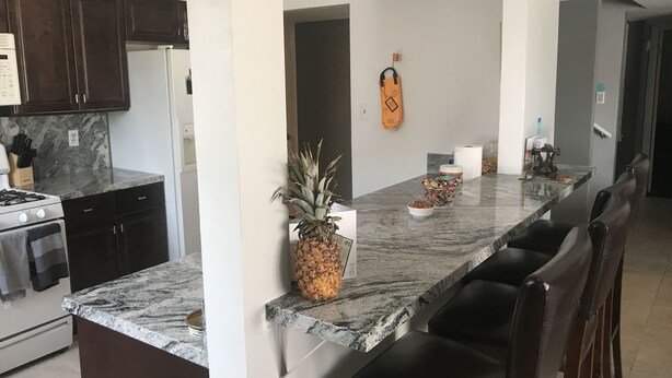 Una cocina moderna con armarios de madera oscura, encimera de granito, estufa a gas y horno empotrado. Hay una isla grande con un bol de aperitivos y una piña.