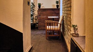 A narrow hallway with a wooden bench, potted plants, and a brick wall.