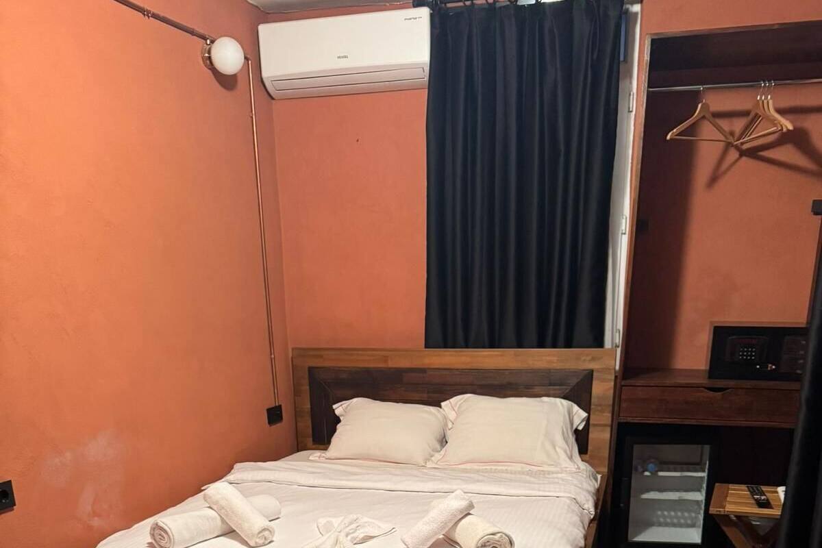 A neatly made bed with pillows and towels, a wooden headboard, a small bedside table with a remote control, and a wall-mounted air conditioner.