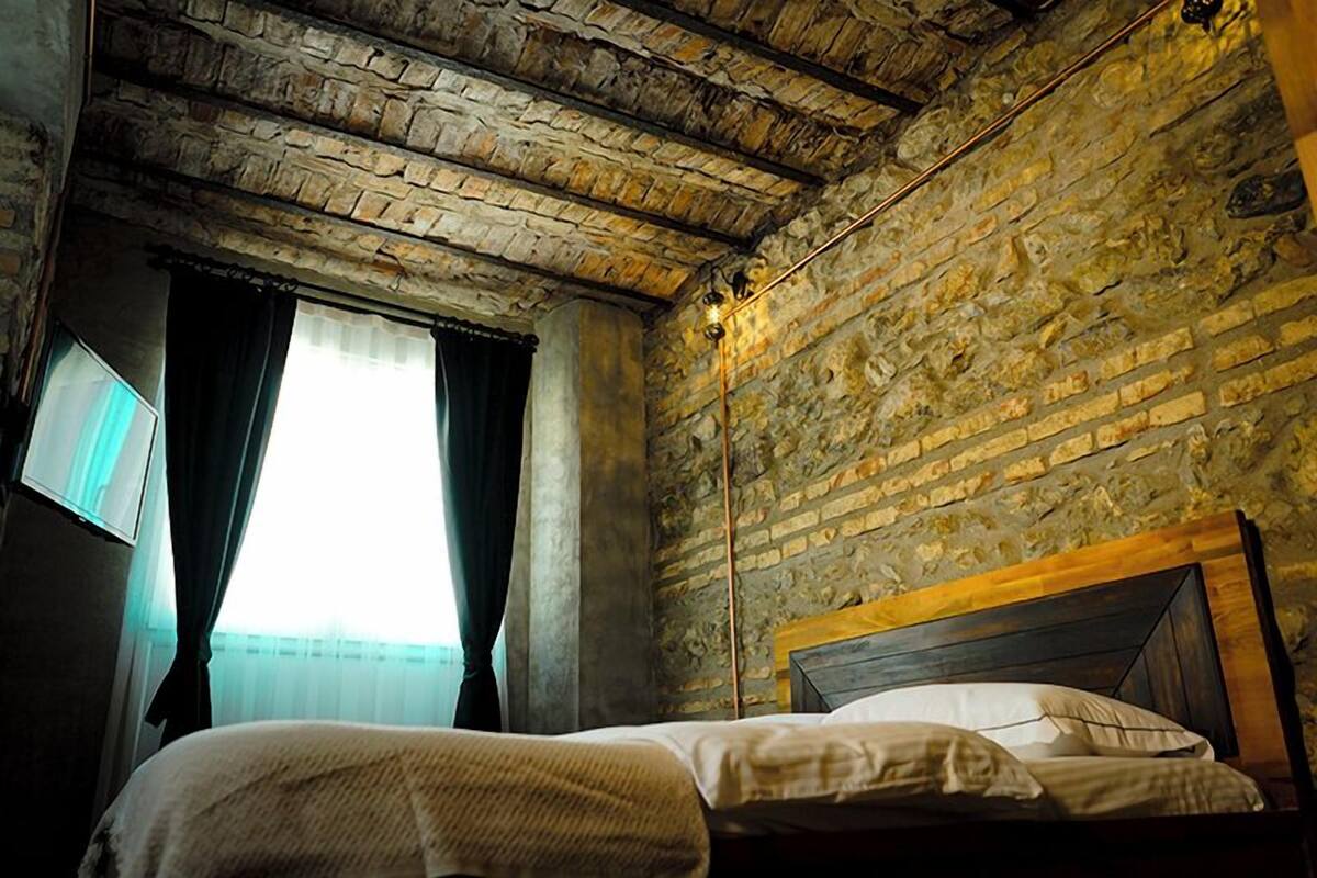A room with a rustic stone wall, a wooden ceiling, and a bed with white bedding.
