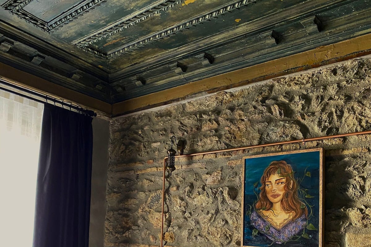 A bedroom with a stone wall, a wooden bed, a nightstand, and a painting.