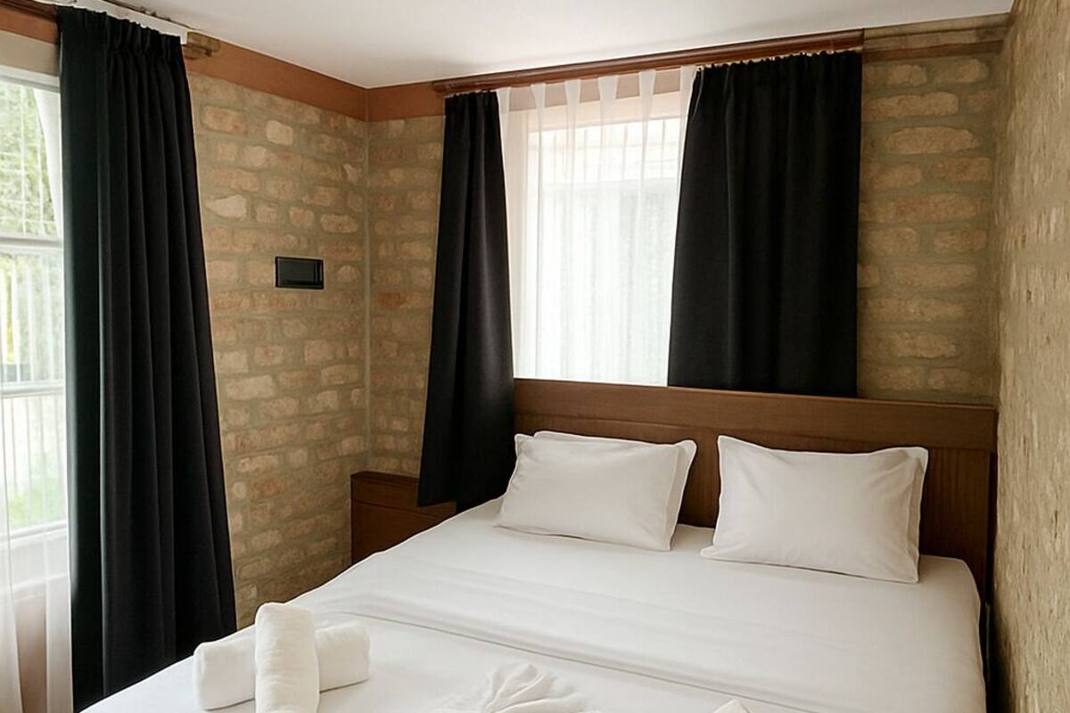 A neatly made bed with white linens and towels, a wooden headboard, and a stone wall.