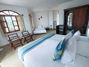 A hotel room with a large bed, a wooden chair, a small table, and a window with curtains.