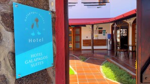 A hotel entrance with a sign for Hotel Galapagos Suites, a reception area, and a patio with outdoor seating. - Hotel Galapagos Suites (Puerto Ayora)