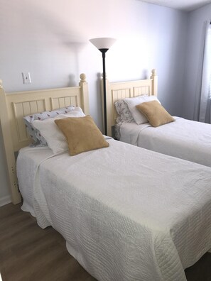 Two single beds with white bedding and brown pillows, a floor lamp, and a plain wall with a light switch. - 3 Bedroom Luxury Oceanfront Condo In Royal Garden Resort (Garden City Beach)