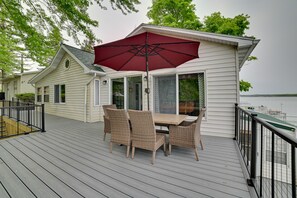 A covered outdoor dining area with a table and chairs, a red umbrella, and a view of the water.