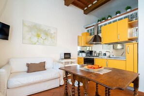 A compact living space with a sofa, a dining table, a kitchen with yellow cabinets, and a mounted TV.