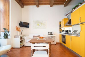 Une cuisine de taille réduite avec des meubles de couleur jaune, une table à manger et un téléviseur fixé au mur.